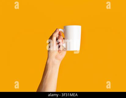 Young man holding cup of hot drink over orange background, close up of hand Stock Photo