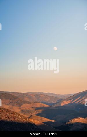 Douro valley terraced hills with a crescent moon visible in the clear sky Stock Photo