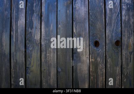 Dark aged wooden fence planks texture featuring prominent natural knots, vertical lines, and round holes, perfect for rustic vintage backgrounds. Stock Photo