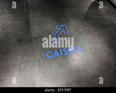 Blue directional arrow and CAISSES lettering on a tiled floor guiding shoppers to checkouts in Paris, France. Stock Photo