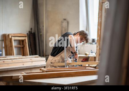 Skillful woman restorer working with wooden details and tools at workbench in restoration workshop Stock Photo