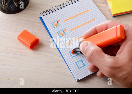 Close-up of an adult hand marking a checklist in a spiral notebook with an orange marker on a desk, symbolizing task completion and productivity. Stock Photo