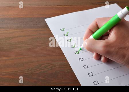Adult hand using a green marker to check items on a paper checklist, representing task completion, organization and workflow management. Stock Photo