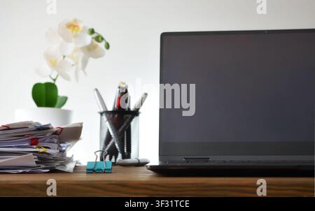 Front view of a laptop on a desk beside stacked documents, office tools, and a plant, illustrating organized work, administration, and professional pr Stock Photo