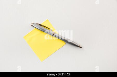 Silver pen placed diagonally on a yellow sticky note over a white background. Simple office and writing concept with clean minimal composition. Stock Photo