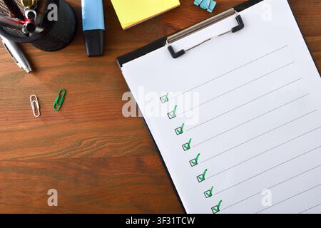 Minimal checklist on a clipboard with green check marks and empty lines, placed on a wooden office desk with stationery and copy space. Stock Photo