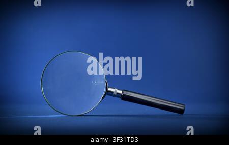 Single magnifying glass on a blue background with copy space, representing search, investigation, focus, observation, and analytical thinking. Stock Photo