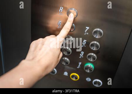 Person pressing the eighth floor button inside a modern elevator. Vertical transportation supports convenient access and efficient movement in Stock Photo