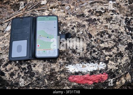 A smartphone displaying a map application rests on a rock marked with a trail sign, indicating a hiking path Stock Photo