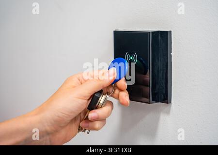 Person using contactless key fob on indoor access control reader. Secure building access protects restricted areas and residential facilities Stock Photo