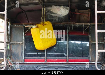 A yellow plastic jerrycan hanging from rear of old pickup truck, weathered metal frame and packed cargo create gritty utilitarian scene with rustic te Stock Photo