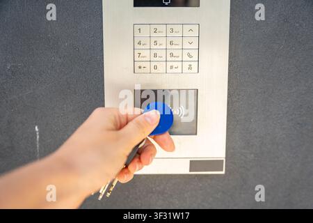 Person using contactless key fob on residential building access control system. Secure entry technology supports convenient and controlled property Stock Photo