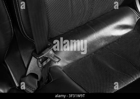 A black leather car seat with perforated fabric and secured seat belt buckle creating focused safety scene with tonal contrast and textured upholstery Stock Photo