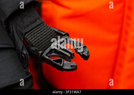 A black plastic buckle clip on nylon strap attached to fabric with orange background conveying functional outdoor gear detail and texture Stock Photo