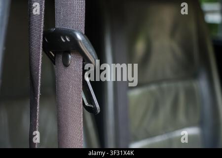 A brown seat belt strap and metal latch hanging inside car interior with leather seat visible and soft light creating calm mood Stock Photo