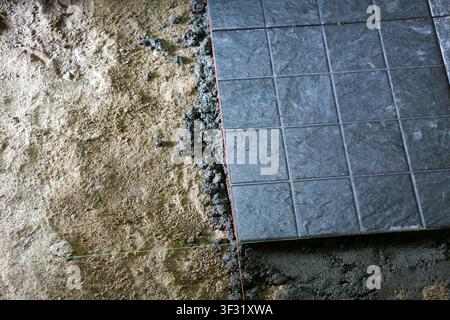 A floor tile installation on prepared mortar bed, gray ceramic tile partially laid over cement mortar with string line guiding alignment, construction Stock Photo