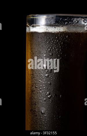 Cold dark beer fills a tall glass with droplets of water on the outside against a dark background from a bar setting Stock Photo