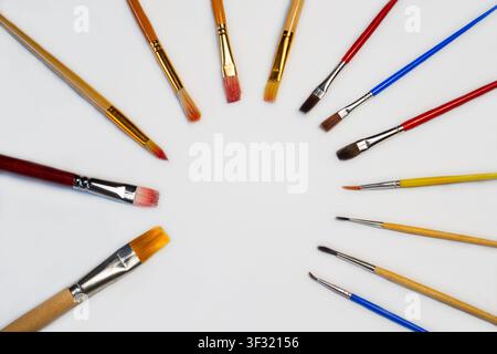 Many paintbrushes are placed in a circle on a plain white surface, ready for use in painting or art projects during the day. Stock Photo