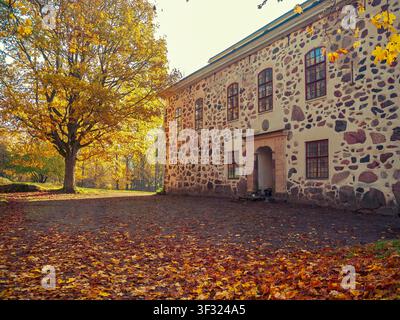 Siuntio, Finland - 14.10.2018: An old stone building stands beside a massive tree with vibrant yellow foliage in a peaceful autumn scene Stock Photo