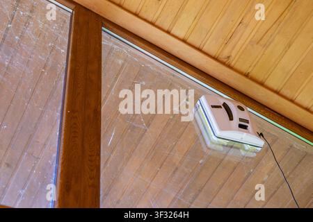 Automatic window cleaning robot working on dirty glass beneath wooden ceiling Stock Photo