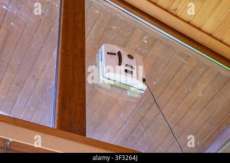 Automatic window cleaning robot working on dirty glass beneath wooden ceiling Stock Photo