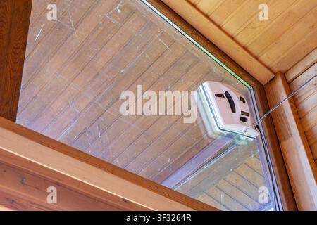 Automatic window cleaning robot working on dirty glass beneath wooden ceiling Stock Photo