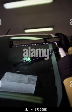 Mechanic cures resin inside windshield crack using lighting equipment. Windshield UV Resin Curing. Windshield repair. Automotive technician holds ultr Stock Photo