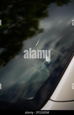 Deep crack visible on the surface of damaged auto glass as the vehicle awaits a professional windshield replacement or resin repair. Stock Photo