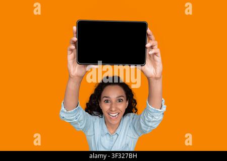 Smiling Woman Holding a Tablet in Front of an Orange Background Stock Photo