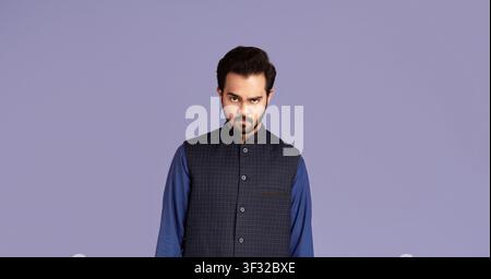 Portrait of strict Indian man in traditional clothes on violet background Stock Photo