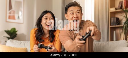 Happy Asian Couple Playing Video Games Together At Home, Joyful Expression, Family Concept Stock Photo