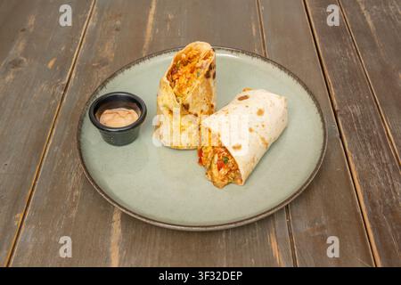 Chicken Tinga Burrito Sliced in Half, Filled with Rice and Tomato, Served with Chipotle Crema Stock Photo