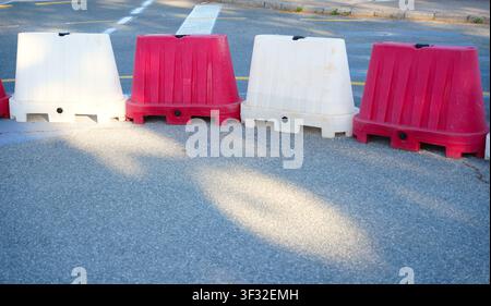 Line of alternating red and white plastic water-filled traffic barriers blocking an asphalt road. Stock Photo