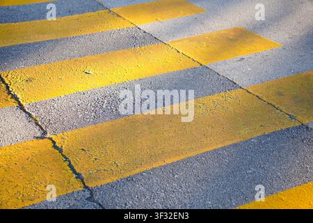 Close-up of temporary yellow pedestrian crossing paint stripes on a cracked asphalt road surface. Stock Photo