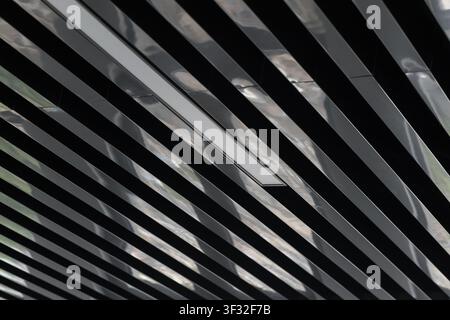 Close-up view of a modern black metallic slatted ceiling showing reflective strips, recessed lighting and a repeating linear pattern evoking industria Stock Photo