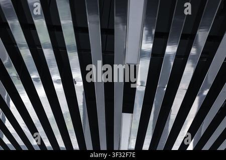 High-contrast close-up of a modern metallic slatted ceiling showing reflective strips, recessed lighting and a repeating linear pattern evoking indust Stock Photo