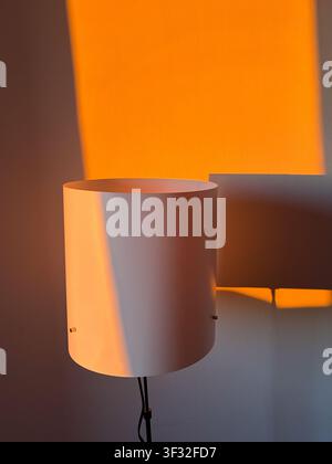 Minimal white floor lamp casting dramatic orange sunlight shadows on a white wall Stock Photo