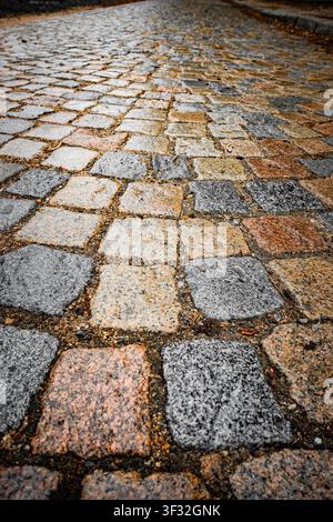 Low-angle close-up of an old uneven cobblestone street, showing weathered stone blocks, texture and perspective Stock Photo