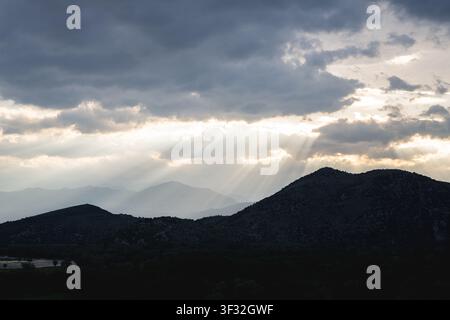 Dramatic mountain range silhouetted against a cloudy sky with golden sun rays breaking through the clouds, cinematic natural landscape. High quality p Stock Photo