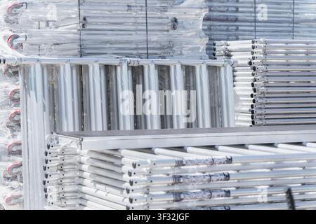 Industrial metal scaffolding frames with red caster wheels neatly stacked and wrapped in protective plastic film at a building logistics depot Stock Photo