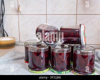 Red cherry jam in multiple glass jars on light kitchen background, organic homemade berry marmalade preserve, side view food composition Stock Photo