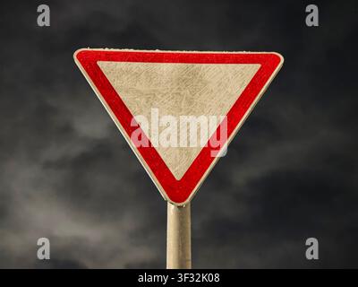 A traffic sign indicates yield rules in a busy urban area with a cloudy sky in the background. The scene captures the city atmosphere. Stock Photo