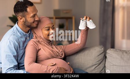 Happy African American Couple Expecting Baby, Holding Shoes Together At Home, Family Concept Stock Photo