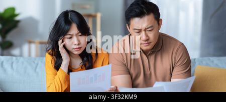 Worried Asian Couple Analyzing Financial Reports At Home, Business Concept Stock Photo