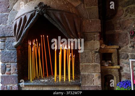 Yellow beeswax candles burn brightly inside a rustic stone alcove, creating a serene spiritual atmosphere at the historic Taxiarches Monastery in Lesb Stock Photo