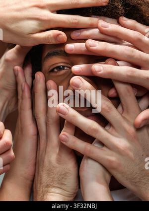 Close up of young back male peering through numerous caucasian hands Stock Photo
