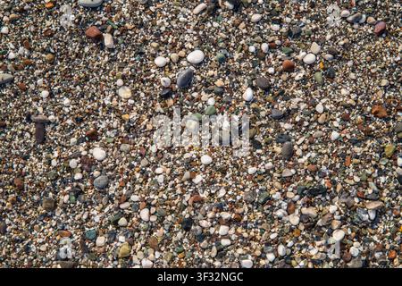 Close-up of a colorful pebble beach with small wet stones and coarse sand. Natural seaside texture and abstract background with multicolored pebbles Stock Photo