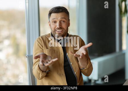 Smiling Young Caucasian Man Gesturing With Hands In Office, Business Communication Concept Stock Photo
