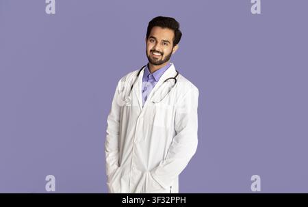 Portrait of confident Indian medical doctor in lab coat looking at camera on violet background Stock Photo