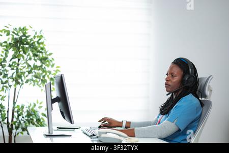 Black medical assistant wearing headset taking calls in customer service Stock Photo